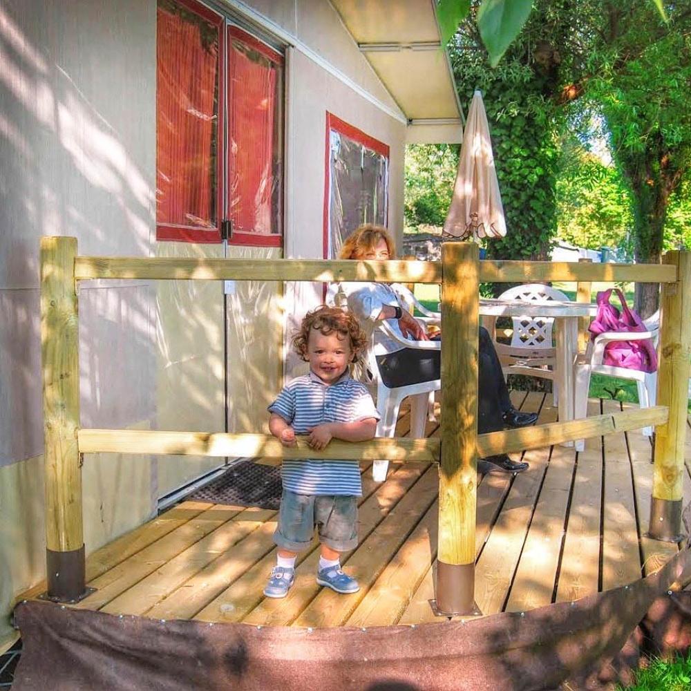 Bambino felice su terrazza di legno, giorno soleggiato, natura intorno.